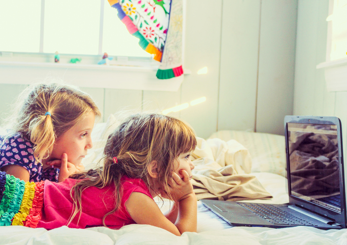 Two little girls laying down and watching something on a laptop